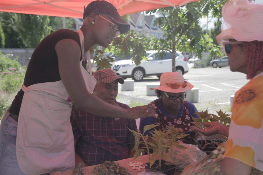 Jhane Thomas, WEHDC/Sankofa’s Market Manager assists vendors Teo and Margarita at the Saturday Marketspace. 