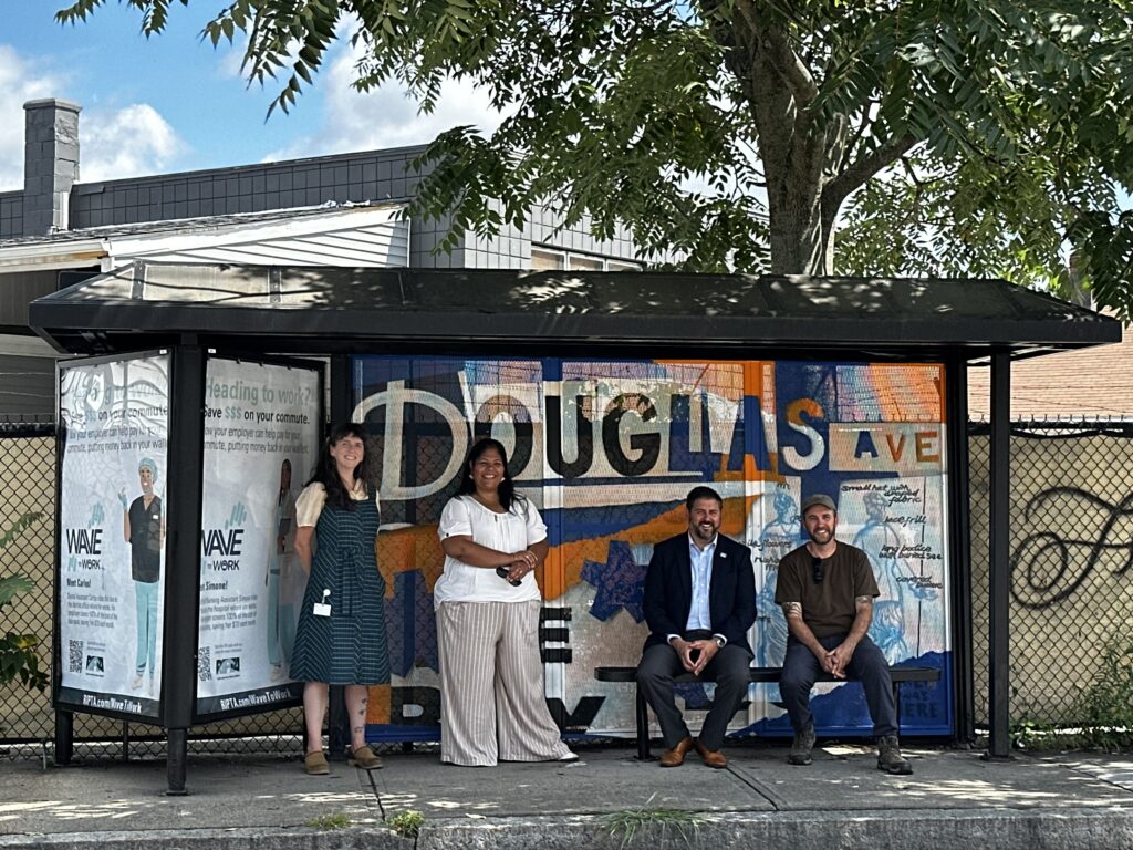 Elected officials and other workers pose in front of the Douglas Ave mural bus shelter.